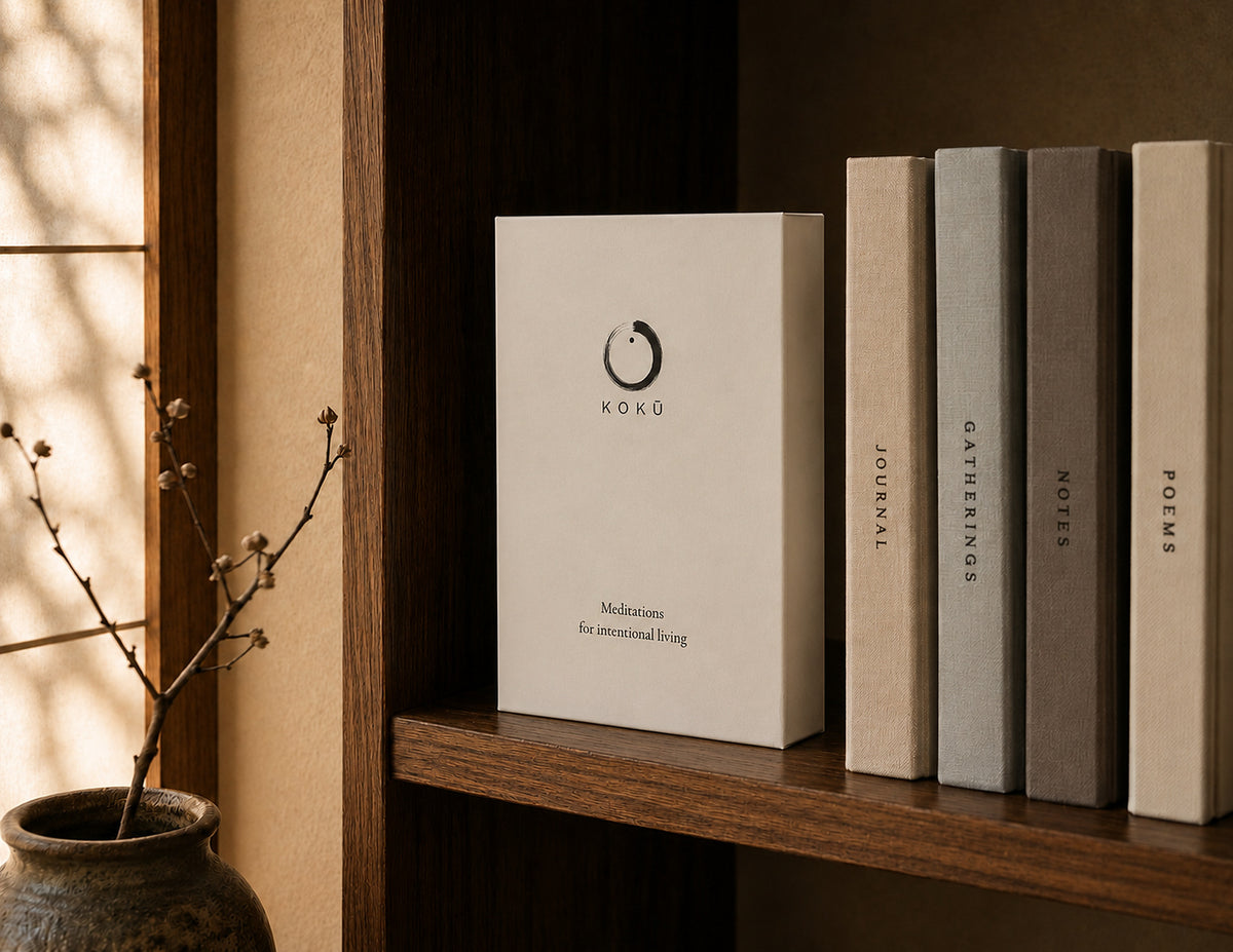 The Kokū book-style keepsake box standing on a wooden shelf beside a row of books, its cover showing a hand-painted ensō, in warm natural light.